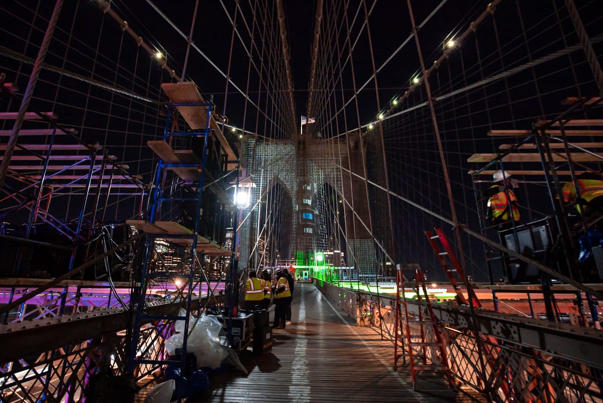 Night install on the Brooklyn Bridge — projection rig and crew in place on the walkway.